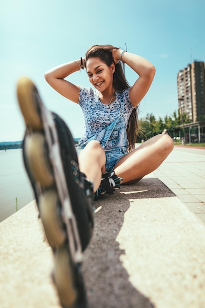 Jovem patinadora está desfrutando na margem do rio da cidade e amarra seus rolos em um lindo dia de verão.