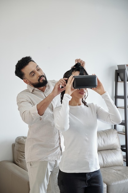 Jovem pedindo ajuda ao namorado para usar óculos de realidade virtual