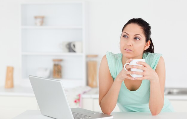 Jovem pensativa com laptop e café