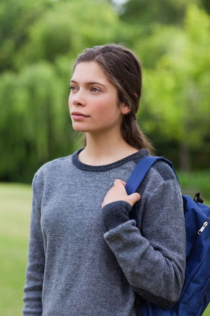 Jovem pensativa de pé no campo enquanto carrega sua mochila