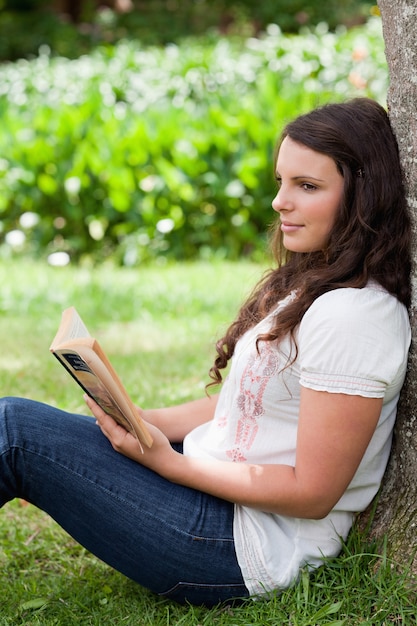 Jovem, pensativa, menina, encostada, árvore, enquanto, lendo, livro