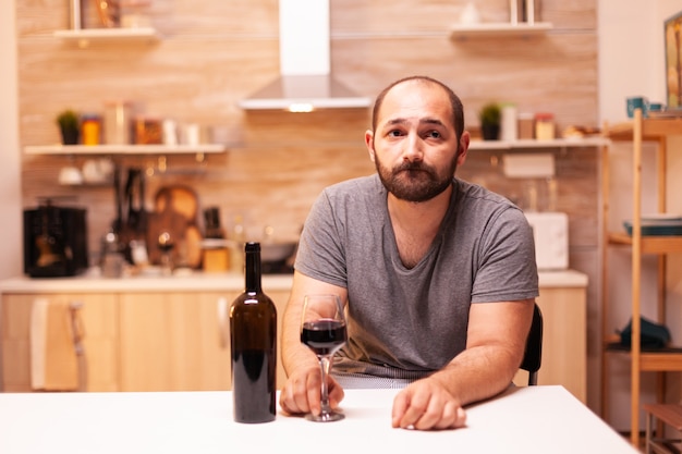 Jovem pensativo segurando uma taça de vinho tinto pensando nos problemas da vida