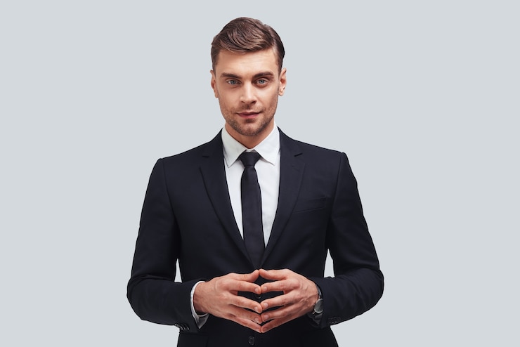 Foto jovem perfeccionista. jovem bonito com roupa formal, de mãos dadas e olhando para a câmera com um sorriso em pé contra um fundo cinza