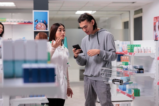 Jovem perguntando ao farmacêutico sobre caixas de medicamentos e comprimidos no smartphone, mostrando o pacote de medicamentos específicos no celular. Cliente e especialista falando sobre produtos farmacêuticos.