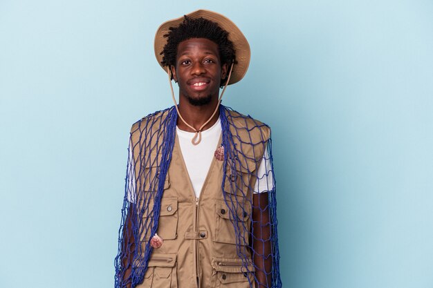 Jovem pescador afro-americano segurando uma rede isolada no fundo azul feliz, sorridente e alegre.