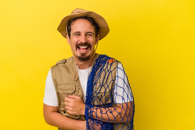 Foto jovem pescador caucasiano segurando a rede isolada no fundo amarelo, rindo e se divertindo.