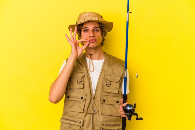 Jovem pescador com maquiagem segurando a haste isolada em um fundo amarelo com os dedos nos lábios, mantendo um segredo.