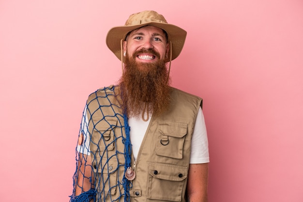 Jovem pescador de gengibre, caucasiano, com barba comprida, segurando uma rede isolada no fundo rosa