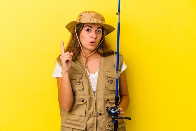 Jovem pescadora caucasiana segurando uma vara isolada em fundo amarelo, tendo uma ótima ideia, o conceito de criatividade.