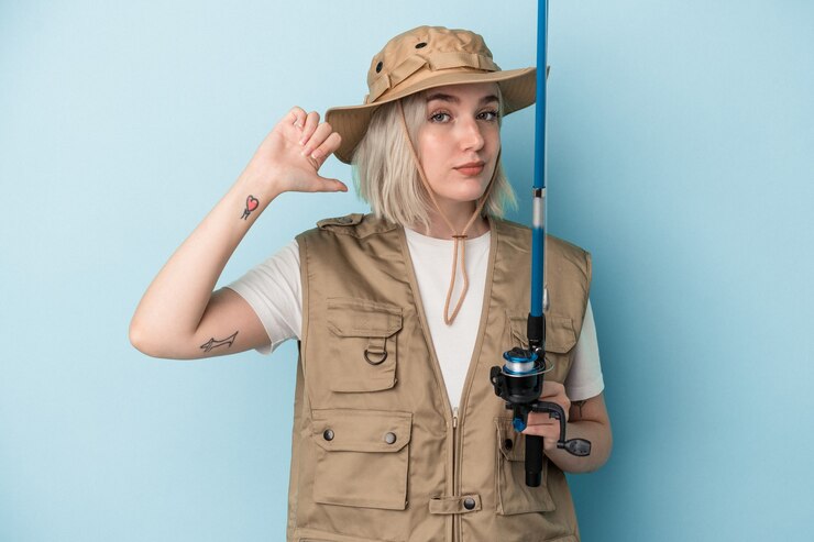 Foto jovem pescadora caucasiana segurando uma vara isolada em um fundo azul se sente orgulhosa e autoconfiante, exemplo a seguir.