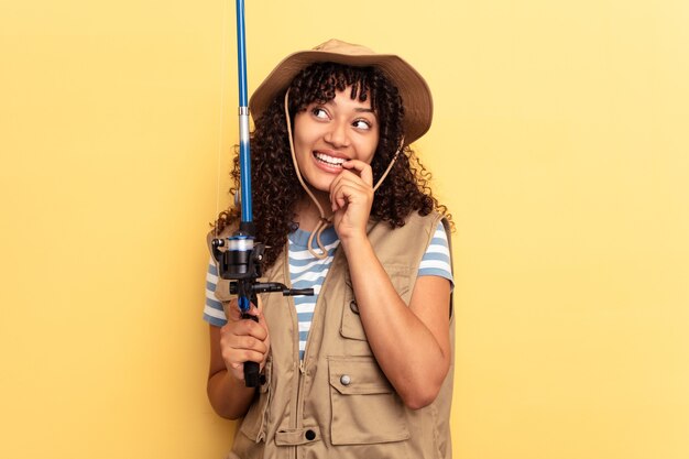 Jovem pescadora de raça mista segurando uma haste isolada em fundo amarelo relaxada pensando em algo olhando para um espaço de cópia.