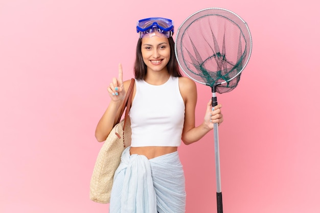 jovem pescadora sorrindo e parecendo amigável, mostrando o número um e óculos de mergulho