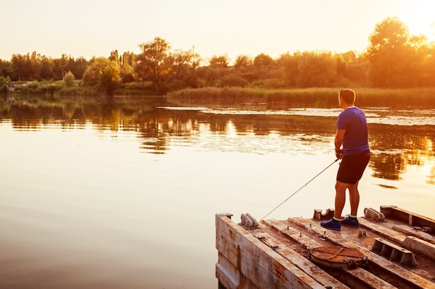 Jovem pescando no rio em pé na ponte ao pôr do sol