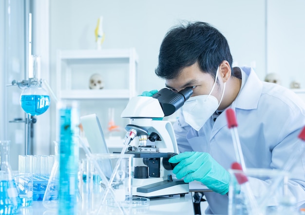 Jovem pesquisador asiático usando microscópio moderno em laboratório.