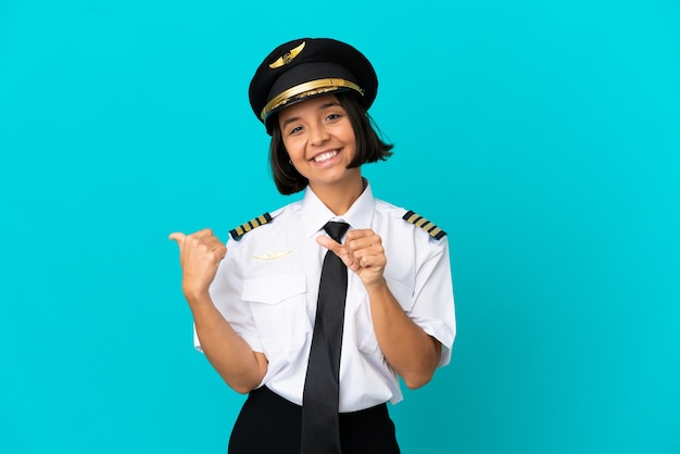 Foto jovem piloto de avião sobre fundo azul isolado apontando para o lado para apresentar um produto