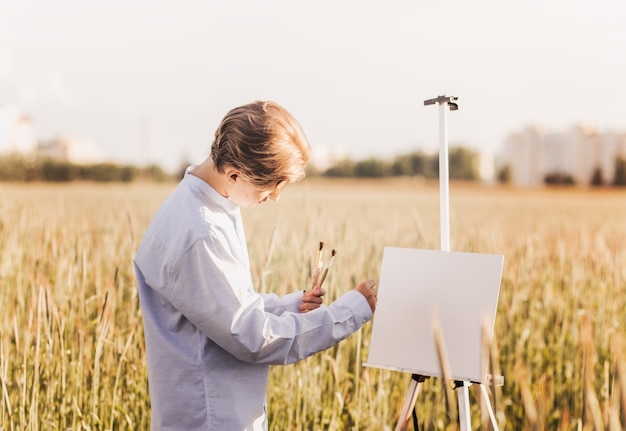 Jovem pinta sobre tela na natureza no verão. Trabalho artístico na natureza. Pleno ar.