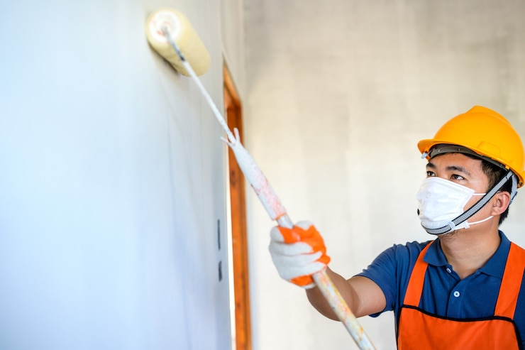 Foto jovem pintor asiático use uma máscara protetora para pintar as paredes internas de branco com um rolo de pintura na nova casa.