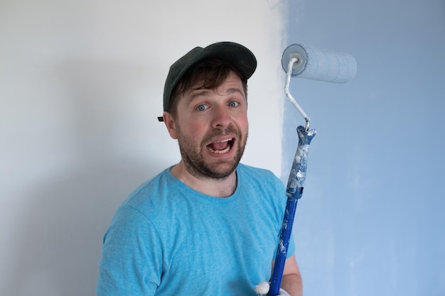 Foto jovem pintor de boné de camiseta azul e luvas pintando uma parede com rolo de pintura