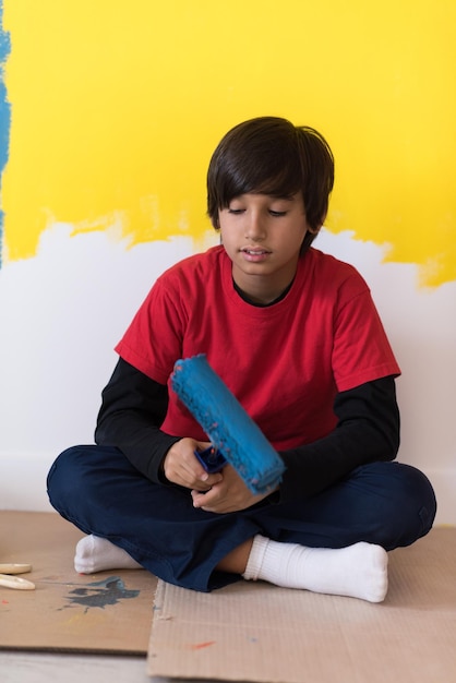 jovem pintor descansando depois de pintar a parede, sentado no chão na nova casa