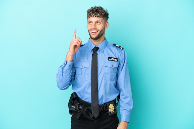 Jovem policial loiro isolado branco sobre fundo azul apontando para cima e surpreso