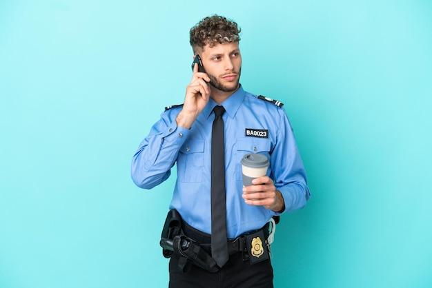 Jovem policial loiro isolado branco sobre fundo azul segurando um café para levar e um celular
