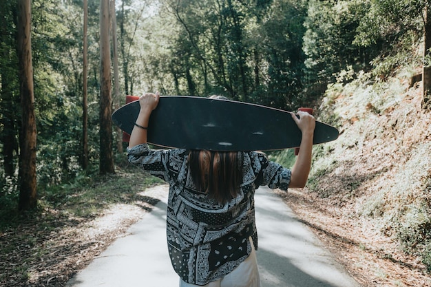 Jovem por trás andando com prancha longa no meio da floresta