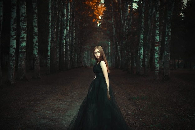 Jovem posando com um vestido preto em uma floresta escura