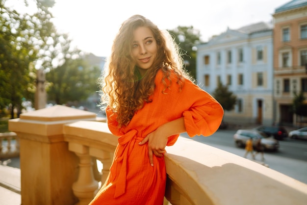 Foto jovem posando contra o pano de fundo da paisagem urbana em vestido laranja brilhante conceito de estilo de vida