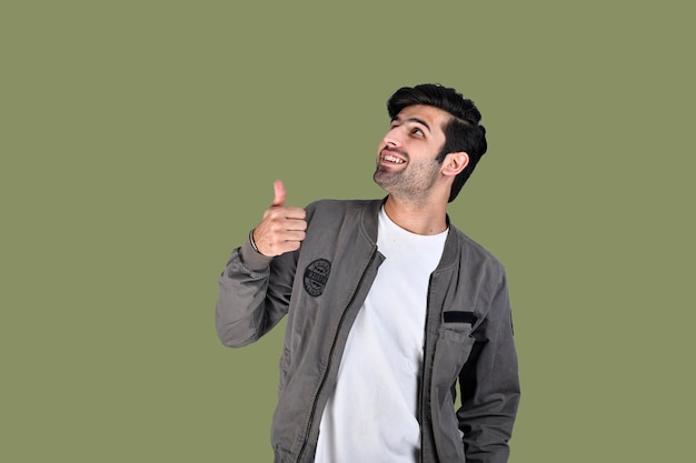 jovem pose frontal vestindo jaqueta polegares para cima com sorriso no fundo verde modelo indiano do paquistanês