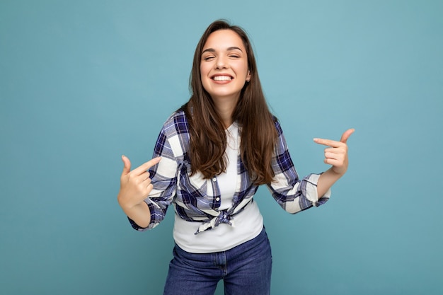 Jovem positiva deliciosa sorridente linda morena com emoções sinceras, vestindo uma camisa quadriculada da moda