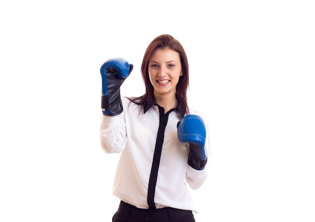 Jovem positiva na camisa branca e calças pretas com cabelos escuros e luvas de boxe azuis sobre fundo branco no estúdio