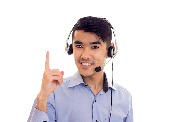 Jovem positivo com cabelo escuro na camisa azul com fones de ouvido pretos sobre fundo branco no estúdio