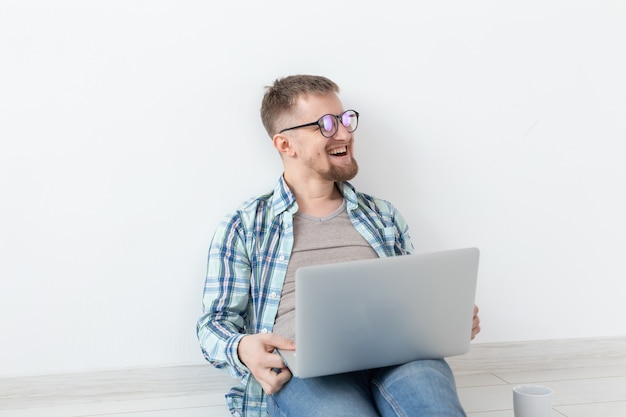 Jovem positivo com roupas casuais e óculos, navegando na Internet usando Wi-Fi e um laptop em busca de um imóvel para alugar. Conceito de pesquisa de inauguração de casa e apartamento.