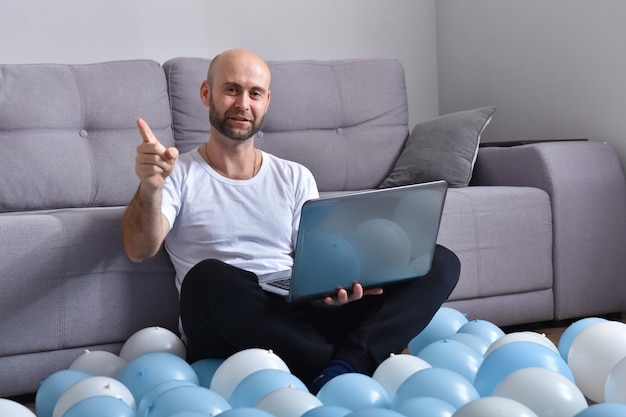 Jovem positivo em roupas casuais, sentado na sala de estar e usando um laptop