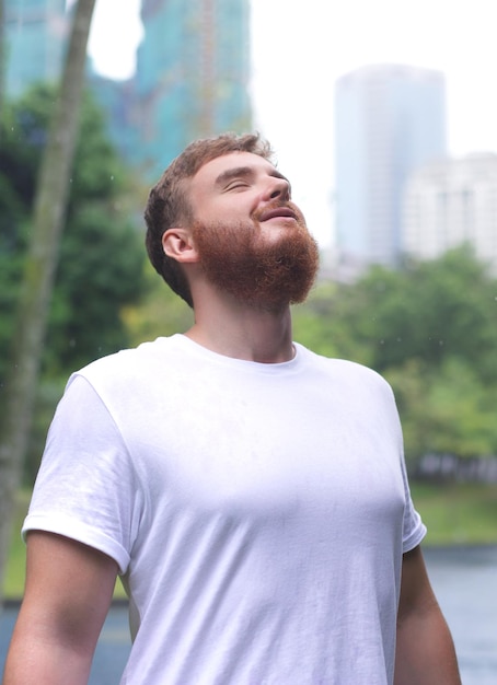 Jovem positivo sorrindo durante a chuva no parque homem alegre curtindo a chuva ao ar livre cara