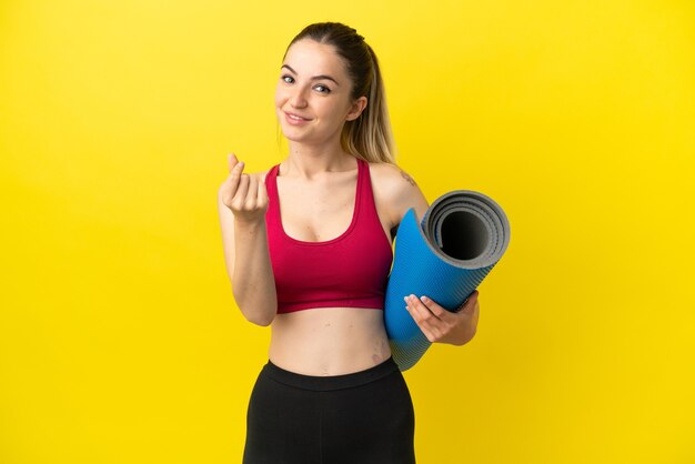 Jovem praticante de esportes indo para aulas de ioga segurando um tapete fazendo gesto de dinheiro