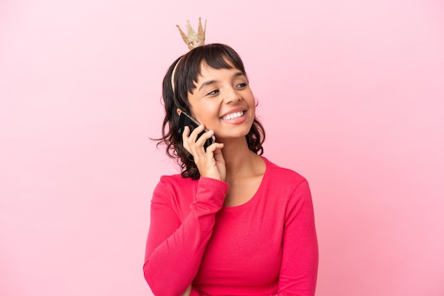 Jovem princesa mestiça com coroa isolada em fundo rosa conversando com o celular