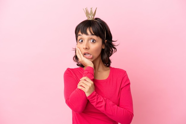 Foto jovem princesa mestiça com coroa isolada em um fundo rosa surpresa e chocada ao olhar para a direita