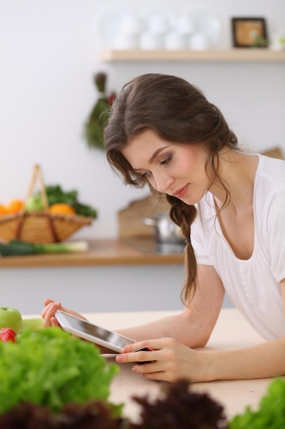 Jovem procurando uma nova receita para cozinhar em uma cozinha. Dona de casa está fazendo compras online por computador tablet e cartão de crédito.