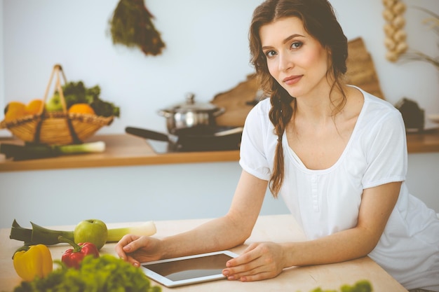 Jovem procurando uma nova receita para cozinhar em uma cozinha. Dona de casa está fazendo compras online por computador tablet e cartão de crédito.