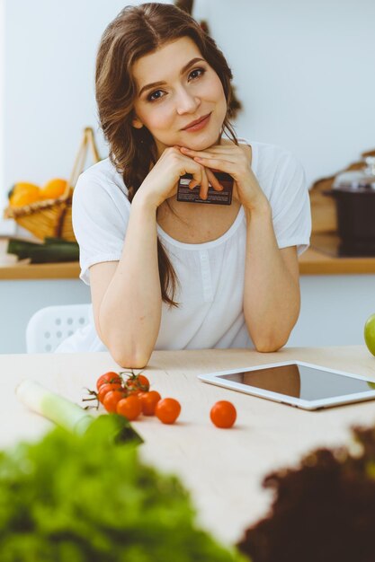 Jovem procurando uma nova receita para cozinhar em uma cozinha. Dona de casa está fazendo compras online por computador tablet e cartão de crédito.