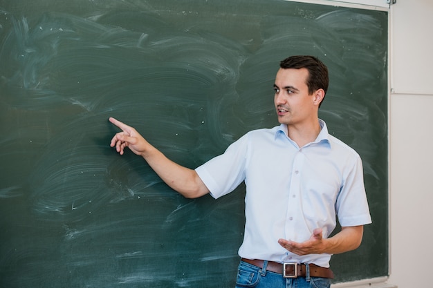 Jovem professor do sexo masculino apontando para a lousa em branco e falando