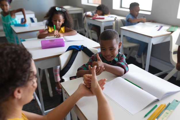 Foto jovem professora caucasiana ensinando linguagem de sinais a um menino afro-americano feliz na aula