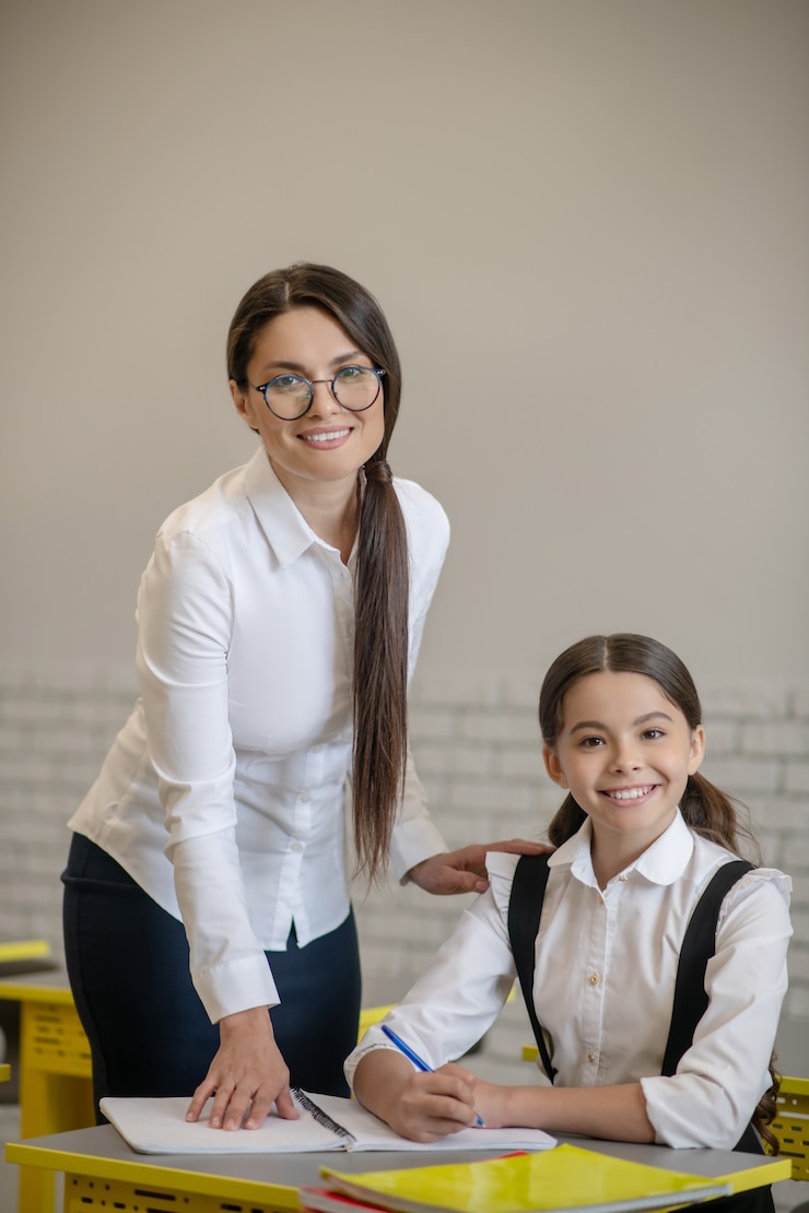 Foto jovem professora de cabelos compridos sorridente e sua simpática aluna feliz na aula durante a aula