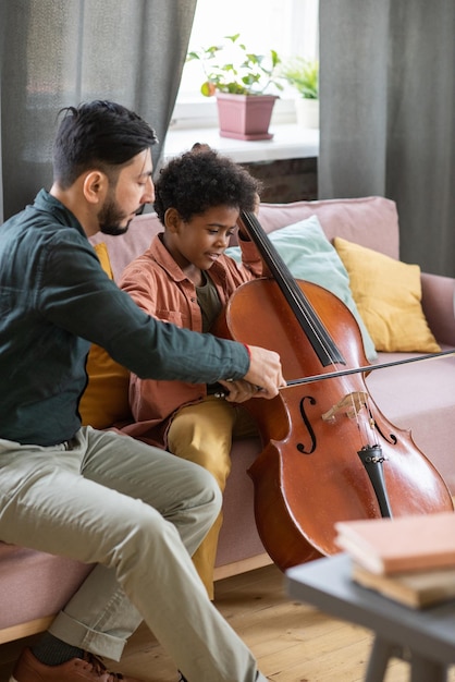 Jovem professora de música ajudando um lindo aluno a tocar violoncelo