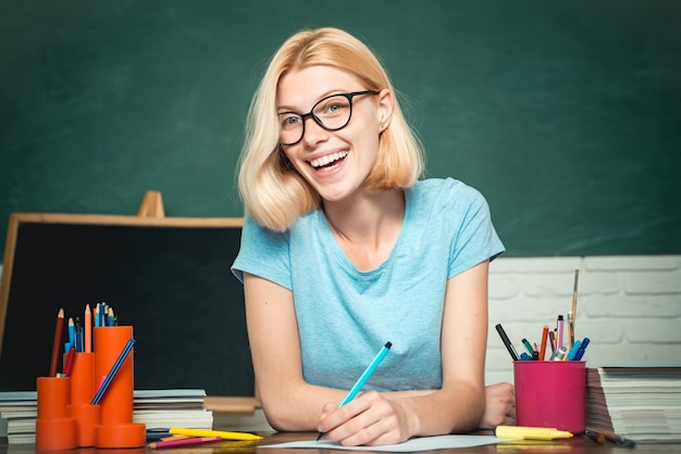 Jovem professora de óculos sobre fundo verde lousa