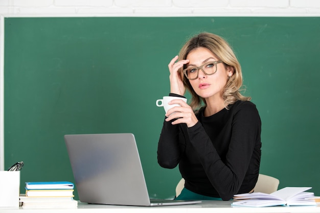 Jovem professora ou aluna tomando café com notebook em uma lousa em branco
