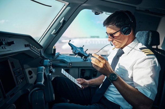 Jovem profissional do sexo masculino com gadgets está sentado no controle da cabine e se preparando para decolar