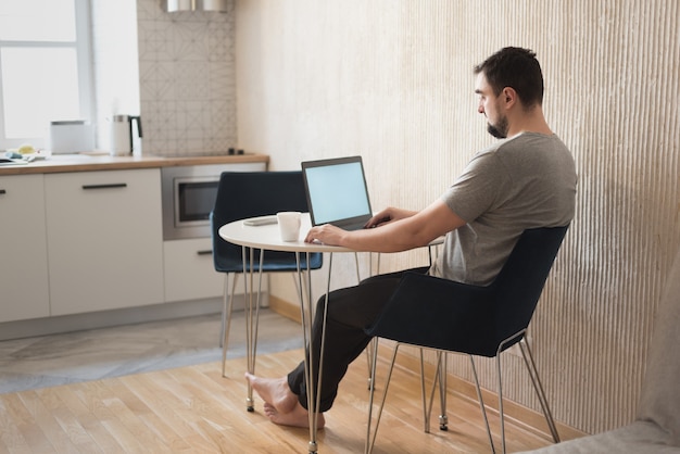 Jovem profissional do sexo masculino usando o computador sentado na mesa de casa. Freelancer ocupado trabalhando em casa.