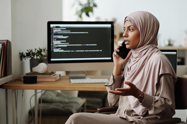 Jovem programadora muçulmana confiante a falar no telemóvel